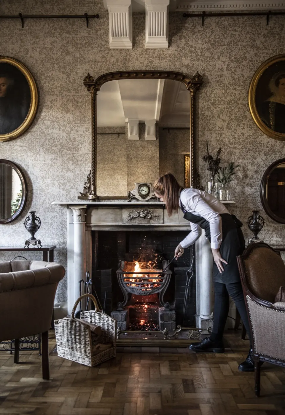 Housekeeper lighting the fire in a hotel drawing room
